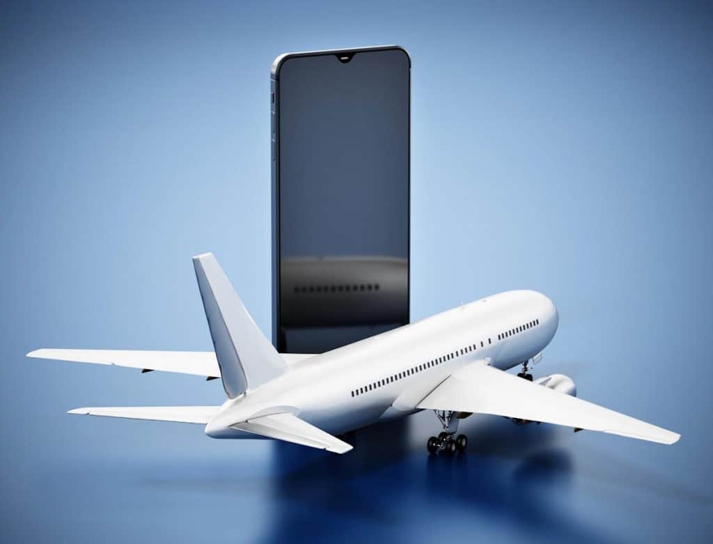 Et modelfly er placeret foran en stor smartphone på en blå baggrund, som symboliserer IATA-vejledninger for lithiumbatterier.