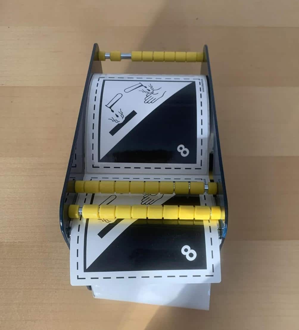 Etiketdispenser 120 mm med gule ruller holder kort med 8 og håndtegninger på en lys træoverflade.