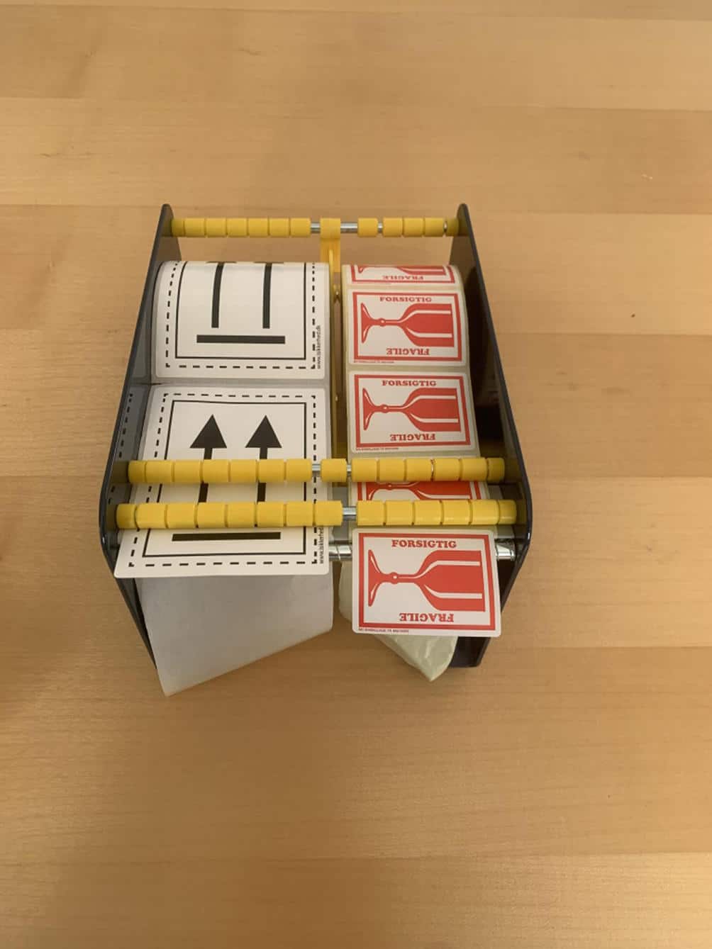 Etiketdispenser 170 mm holder ruller med forsendelsesetiketter og FRAGILE-klistermærker på en træoverflade.